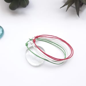 May include: Three friendship bracelets in red, white, and green colors. The bracelets are tied together in a knot.