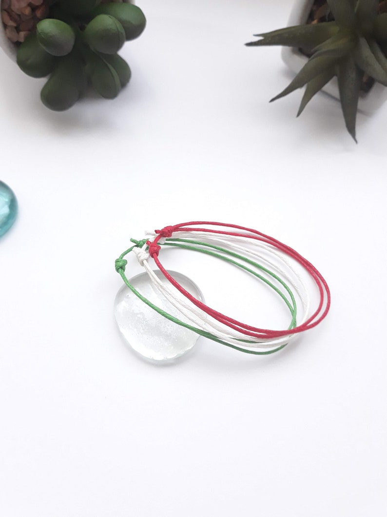 May include: Three friendship bracelets in red, white, and green colors. The bracelets are tied together in a knot.