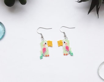 May include: A pair of beaded toucan earrings with silver hooks. The toucans are green, yellow, pink, and white.