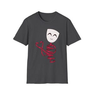 May include: Dark gray t-shirt featuring a whimsical design. The graphic depicts a white mask with a smiling face, connected to a red ribbon that wraps around the body. The ribbon forms a heart shape. The shirt is made of a soft material.