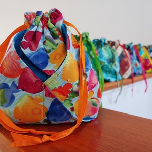 May include: A collection of colorful drawstring bags with various patterns, including a bag with a fish print and orange drawstrings. The bags are displayed on a wooden shelf.