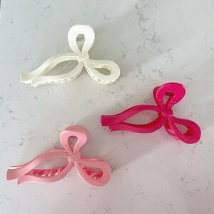 Op de afbeelding: Drie haarclips in de vorm van strikken. E&eacute;n is wit, &eacute;&eacute;n is roze en &eacute;&eacute;n is felroze.