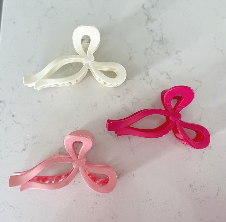 Op de afbeelding: Drie haarclips in de vorm van strikken. E&eacute;n is wit, &eacute;&eacute;n is roze en &eacute;&eacute;n is felroze.