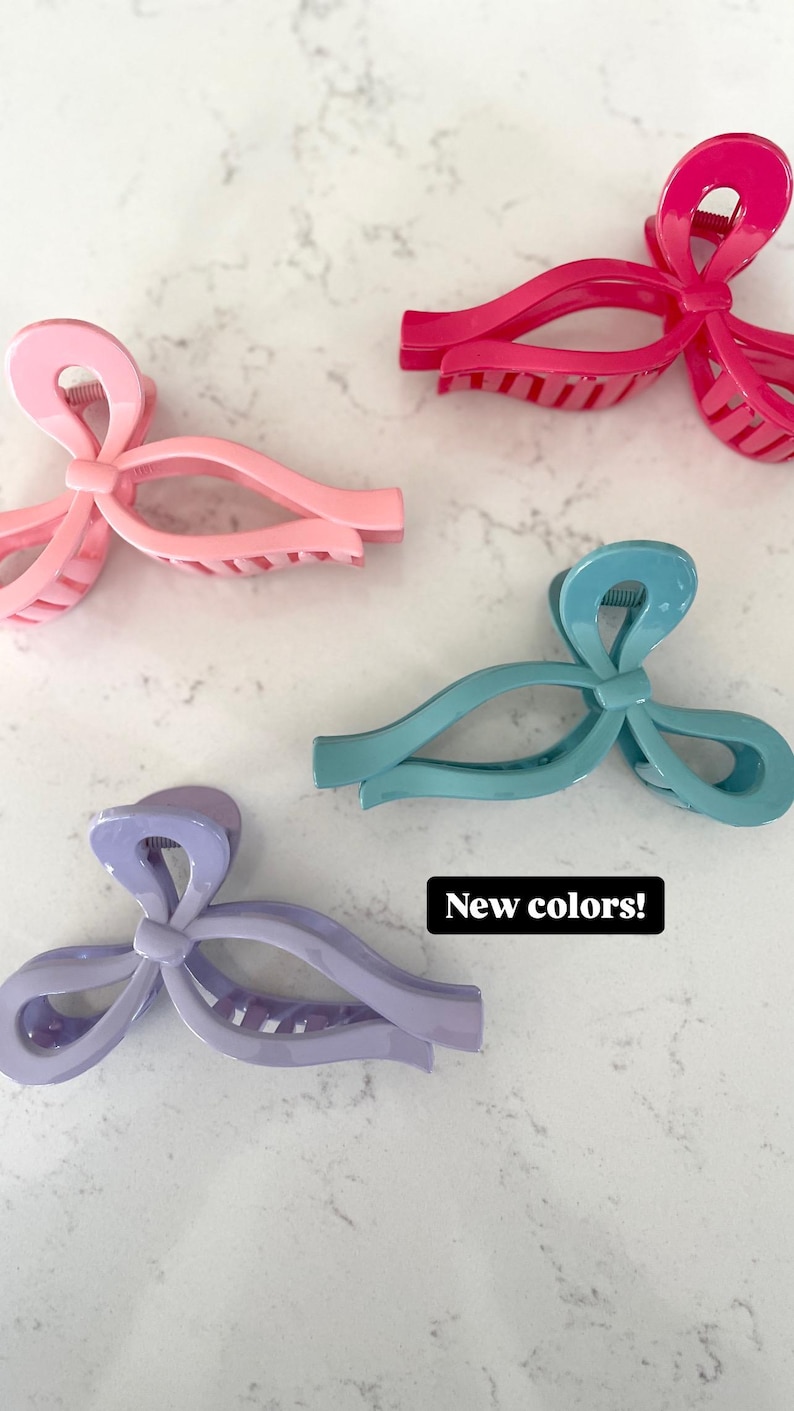 Op de afbeelding: Vier plastic haarclips in verschillende kleuren: roze, paars, teal en felroze. Elke clip heeft de vorm van een strik en een textuur.