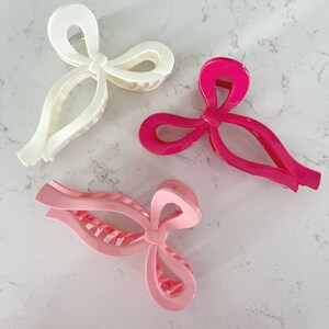 Op de afbeelding: Drie haarclips in de vorm van een strik. E&eacute;n is wit, &eacute;&eacute;n is roze en &eacute;&eacute;n is felroze.