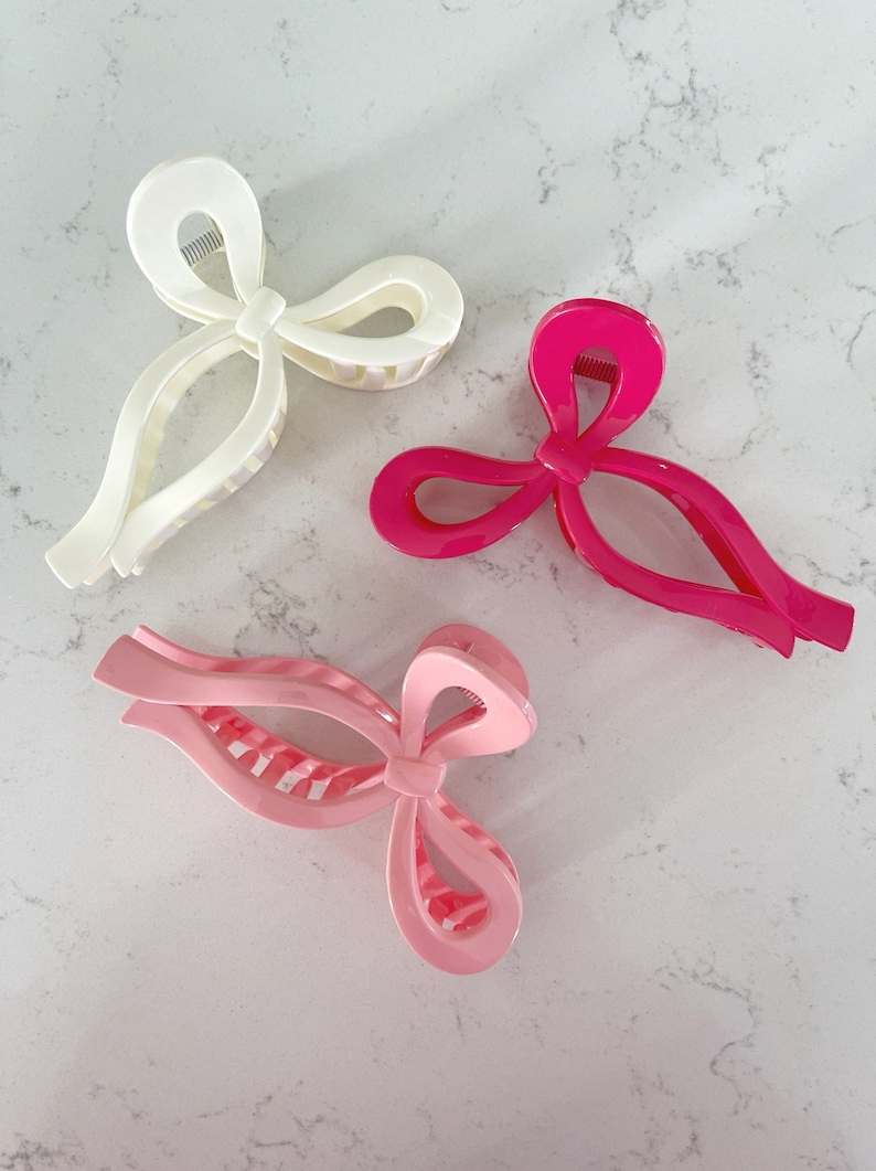 Op de afbeelding: Drie haarclips in de vorm van een strik. E&eacute;n is wit, &eacute;&eacute;n is roze en &eacute;&eacute;n is felroze.