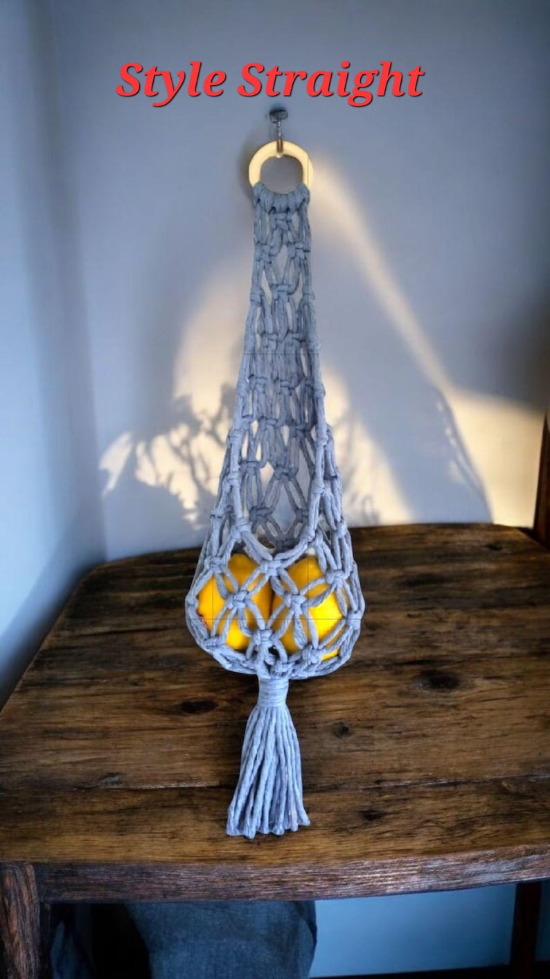May include: A gray macrame fruit hammock with a wooden ring and tassel, holding yellow lemons. The text "Style Straight" is in red at the top. The hammock hangs on a wooden table.
