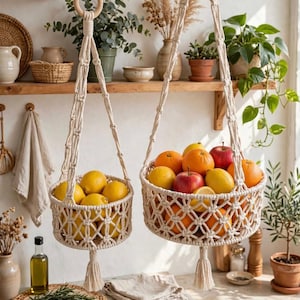 May include: Two off-white macrame hanging baskets with circular wooden rings at the top and decorative tassels at the bottom. The smaller basket holds yellow lemons, while the larger basket is filled with oranges, red apples, and yellow lemons.
