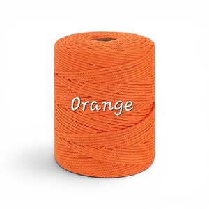 May include: A cylindrical spool of bright orange macrame cord wound tightly in a continuous spiral pattern. The word Orange is printed in white script font across the center of the spool, which features a hollow circular core at the top.