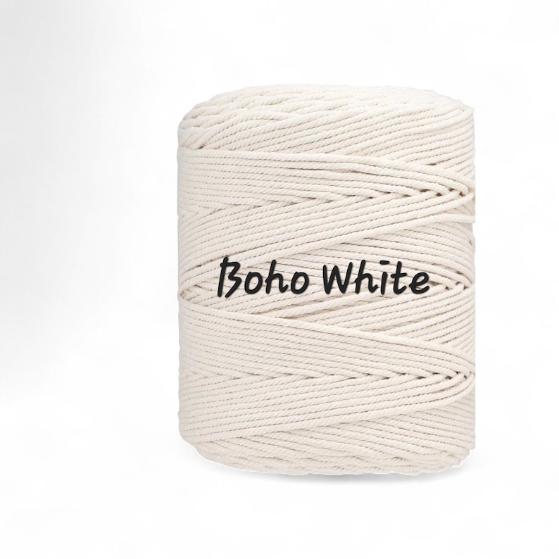 May include: A cylindrical spool of off-white macrame cord wound in a continuous spiral pattern. The text "Boho White" is printed in black, sans-serif lettering across the center of the cord spool, which features a textured, braided surface.