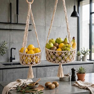 May include: Two off-white macrame hanging baskets suspended by knotted cords from wooden rings. The smaller basket holds yellow lemons, while the larger basket contains a variety of green apples, pears, bananas, kiwis, and green grapes.