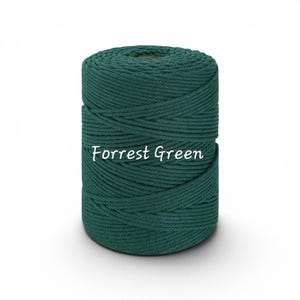 May include: A cylindrical spool of dark green macrame cord wound in a tight, continuous spiral pattern. The text "Forrest Green" is printed in white, cursive lettering across the center of the spool, clearly visible against the dark cord.