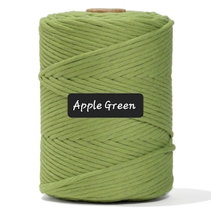 May include: A large spool of apple green macrame cord. The cord is tightly wound and has a textured appearance. A black label with the words "Apple Green" is visible on the front of the spool. The background is plain white.