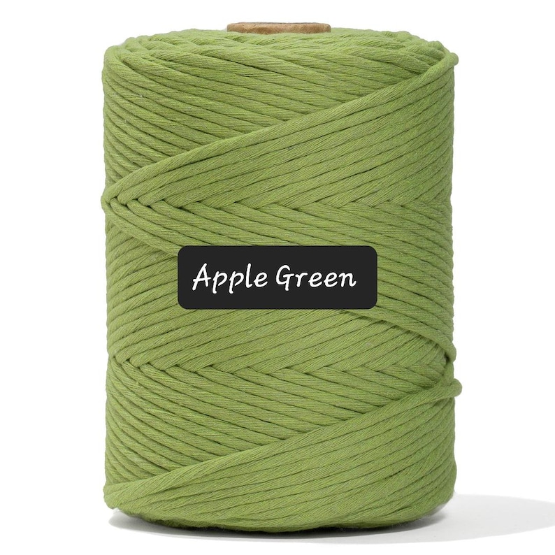 May include: A large spool of apple green macrame cord. The cord is tightly wound and has a textured appearance. A black label with the words "Apple Green" is visible on the front of the spool. The background is plain white.