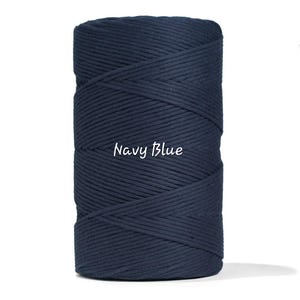 May include: A tightly wound spool of navy blue macrame cord. The text "Navy Blue" is written in a cursive font across the front of the spool. The cord is a solid, dark blue color.