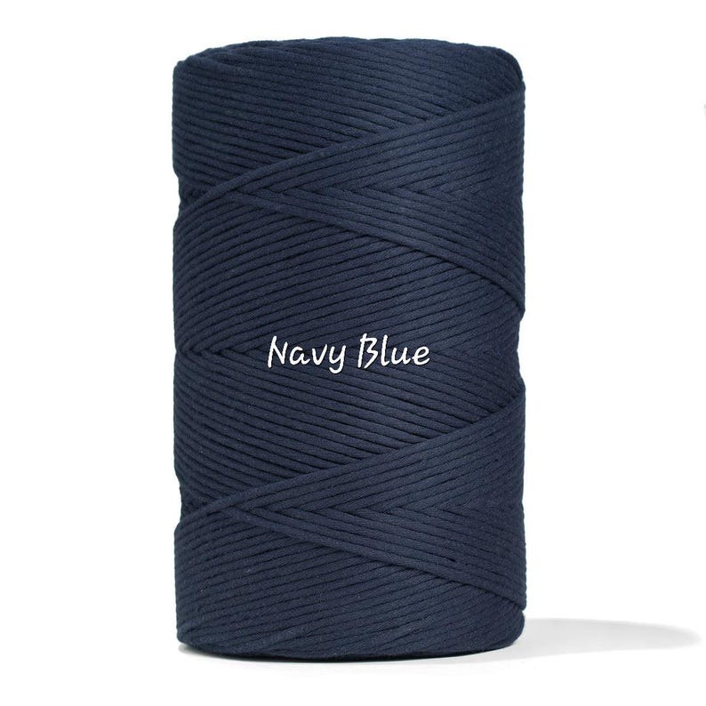 May include: A tightly wound spool of navy blue macrame cord. The text "Navy Blue" is written in a cursive font across the front of the spool. The cord is a solid, dark blue color.