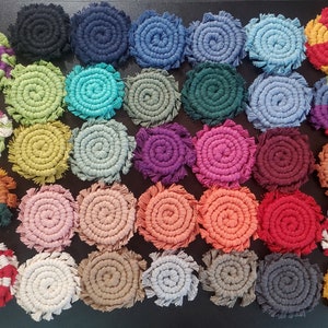 May include: A collection of 30 colorful crocheted coasters with various patterns and colors, including red, blue, green, yellow, orange, purple, and white. The coasters are made with a thick, textured yarn and have a fringed edge.