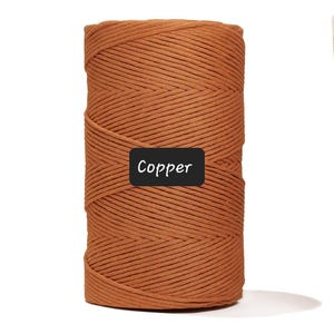 May include: A spool of copper-colored macrame cord. The cord is tightly wound and has a textured appearance. The word "Copper" is displayed on a black label.