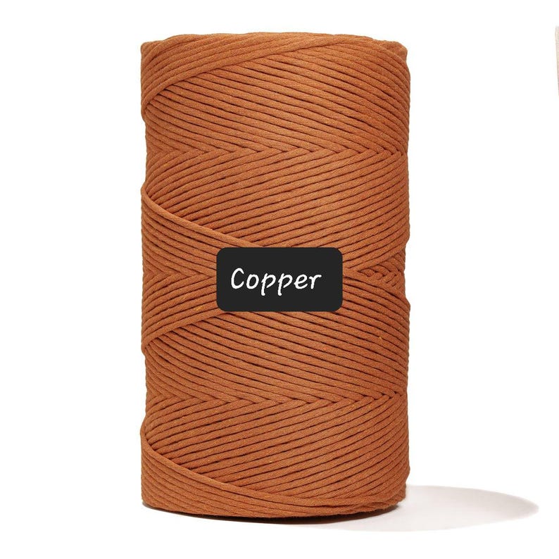 May include: A spool of copper-colored macrame cord. The cord is tightly wound and has a textured appearance. The word "Copper" is displayed on a black label.