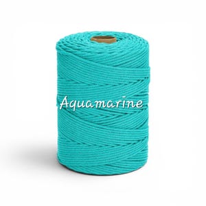 May include: A cylindrical spool of aquamarine colored cord wound in a tight, continuous spiral pattern. The word Aquamarine is printed in white script across the center of the spool, which features a brown cardboard core at the top center.