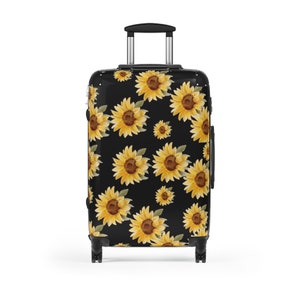 May include: Black suitcase with a sunflower pattern. The sunflowers are yellow with brown centers and green leaves. The suitcase has a black handle and four black wheels.
