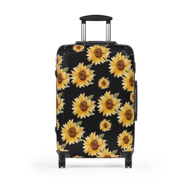 May include: Black suitcase with a sunflower pattern. The sunflowers are yellow with brown centers and green leaves. The suitcase has a black handle and four black wheels.