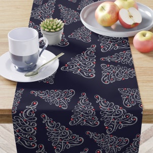 May include: A navy blue table runner with a repeating pattern of white stylized Christmas trees with red ornaments.