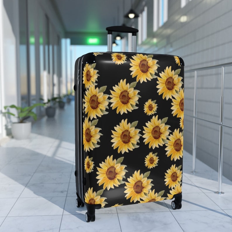 May include: Black suitcase with a sunflower pattern. The suitcase has a retractable handle and four wheels.