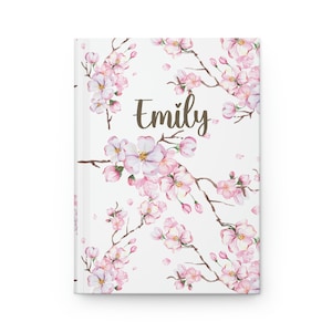 Op de afbeelding: Een wit dagboek met een bloemenontwerp met roze kersenbloesems en de naam "Emily" gedrukt in bruine tekst.