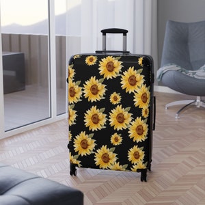 May include: Black suitcase with a sunflower pattern. The sunflowers are yellow with brown centers and green leaves. The suitcase has a black handle and wheels.