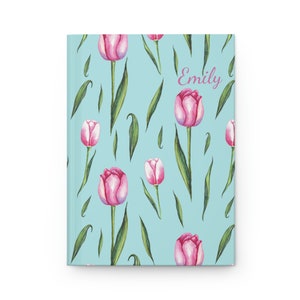 May include: A light blue notebook with a pink tulip pattern and the name "Emily" written in pink on the cover.