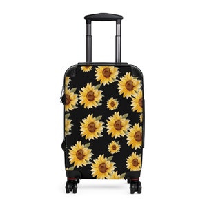 May include: Black suitcase with a sunflower pattern. The sunflowers are yellow with brown centers and green leaves. The suitcase has a retractable handle and four wheels.