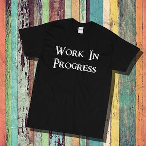 Puede incluir: Camiseta negra con texto blanco que dice "WORK IN PROGRESS".