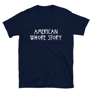 May include: A dark navy blue short-sleeved t-shirt featuring the white text AMERICAN WHORE STORY printed in a stylized, clean font across the center of the chest. The garment has a crew neckline and a standard, straight-cut silhouette.