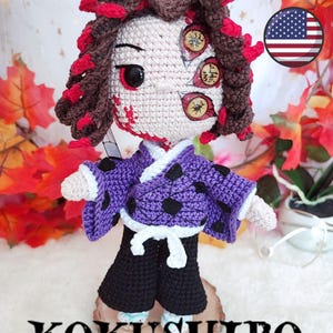 Op de afbeelding: Gehaakte Kokushibo-pop, een personage uit een animeserie. De pop heeft een crèmekleurig gezicht met meerdere ogen, rode markeringen en bruin haar met rode accenten. Ze draagt een paarse kimono met zwarte stippen en een zwarte broek. De tekst "KOKUSHIBO FIRST UPPER MOON" staat onderaan.