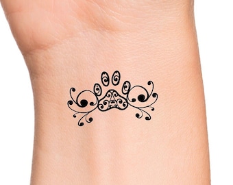 May include: A black paw print tattoo design with decorative swirls on either side.