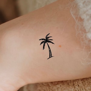 May include: A black palm tree tattoo on a person's arm.