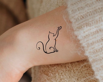 May include: A simple line drawing tattoo of a cat reaching up to a heart. The tattoo is on a person's arm.