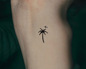 May include: A black palm tree silhouette tattoo with a small airplane flying above it.