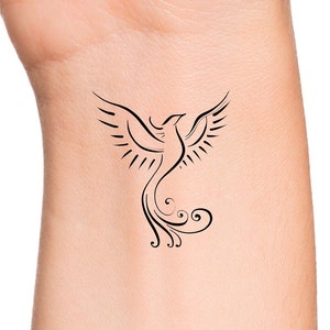 May include: A black line art tattoo design of a phoenix with its wings spread wide. The phoenix is stylized with a long, flowing tail.