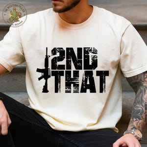 Op de afbeelding: Crèmekleurig T-shirt met de tekst "2ND THAT" in een verweerde, zwarte lettertype, met een zwarte geweer afbeelding. Het shirt heeft een ronde hals en korte mouwen. Het logo van The Western File Co. is zichtbaar linksboven.