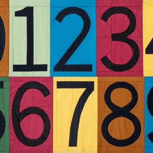 May include: A colorful patchwork of fabric squares, each displaying a large black number from 0 to 9. The background colors include brown, green, blue, red, and yellow. The numbers are bold and outlined in black.