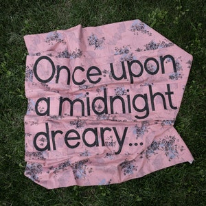 May include: A pink fabric banner with a floral pattern and the text "Once upon a midnight dreary..." printed in black.