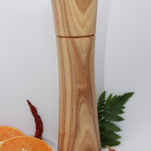 K&ouml;nnte beinhalten: Eine Pfefferm&uuml;hle aus Holz mit einer nat&uuml;rlichen Holzmaserung. Die M&uuml;hle ist hoch und schlank mit einem abgerundeten Kopf. Sie steht auf einer wei&szlig;en Oberfl&auml;che mit Orangenscheiben, roten Chilischoten und schwarzen Pfefferk&ouml;rnern.
