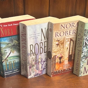 May include: A collection of hardcover books by Nora Roberts, featuring various cover designs. Titles include "Rebellion", "Betrayal", and "Finding the Dream". The spines display the author's name in a bold font, with the book titles below.