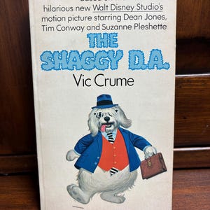 May include: Vintage book cover for "The Shaggy D.A." by Vic Crume. The cover features a cartoon dog in a suit and hat, holding a briefcase. Text includes the title and author's name, along with the film's cast.