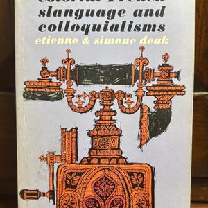 May include: A vintage paperback book titled "A Dictionary of Colorful French Slanguage and Colloquialisms" by Etienne & Simone Deak. The cover features an orange illustration of a telephone on a light purple background. The book is a Dutton paperback original.