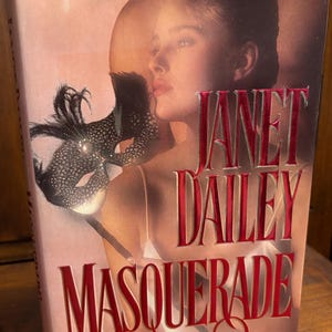 May include: A paperback book titled "Masquerade" by Janet Dailey. The cover features a woman with a mask and a soft pink background. The title and author's name are in a bold, red font.