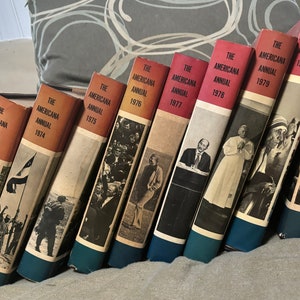 May include: A collection of ten hardcover books, all titled "The Americana Annual" with a year ranging from 1972 to 1981. The books are arranged in a staggered stack, with the oldest book on the left and the newest book on the right.
