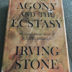 May include: A vintage paperback book titled "The Agony and the Ecstasy", the biographical novel of Michelangelo, by Irving Stone. The cover is brown with a faded, mottled appearance.